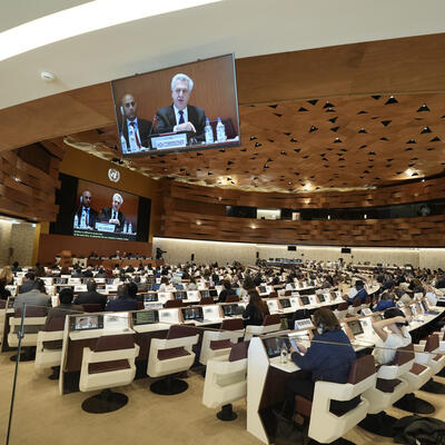 A modern conference room filled with attendees, facing large screens that display speakers at the front during a formal meeting of the UNHCR Executive Committee.