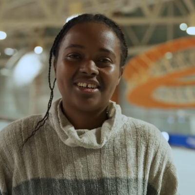 Person standing indoors in a modern building with high ceilings and orange architectural elements in the background.