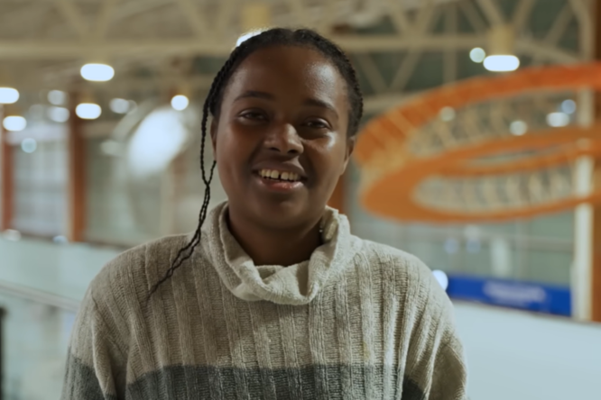 Person standing indoors in a modern building with high ceilings and orange architectural elements in the background.
